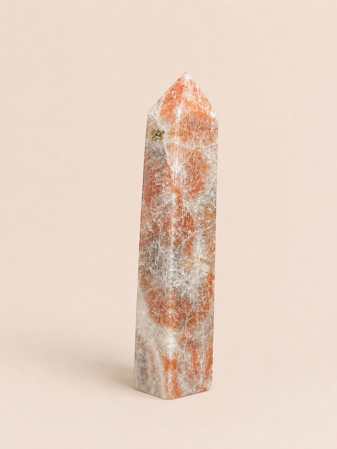 A polished natural moonstone sunstone point with orange and white marbling, standing upright on a solid beige background.