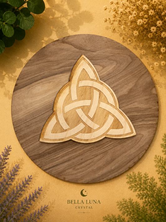 A circular wooden tray or serving board with a natural wood grain finish, featuring a light-colored Celtic triquetra knot design in the center. The board is photographed from above on a textured gold background decorated with dried flowers, green leaves, and lavender sprigs.