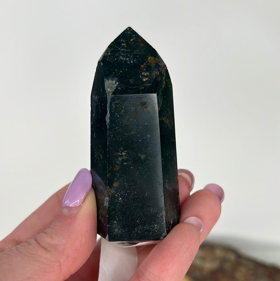 A Baja Jasper Tower crystal with swirling patterns of red, orange, and brown colors, held in a person's hand.