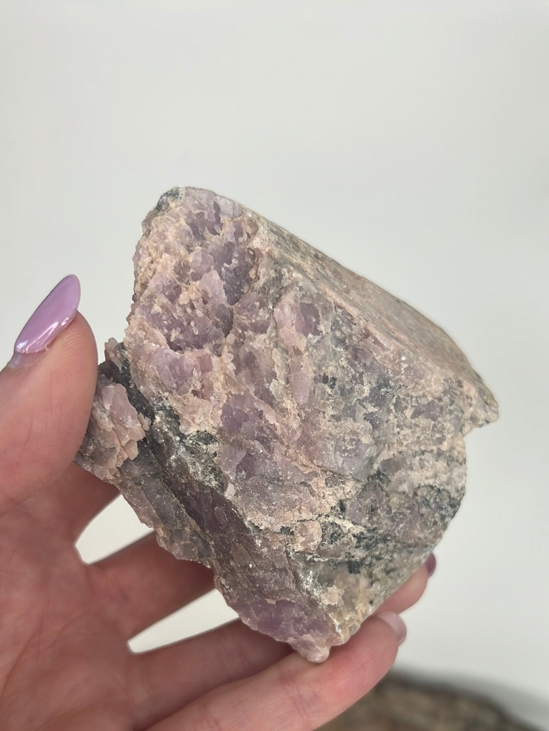 Rough Kunzite mineral specimen with purple coloration, held in a person's hand.